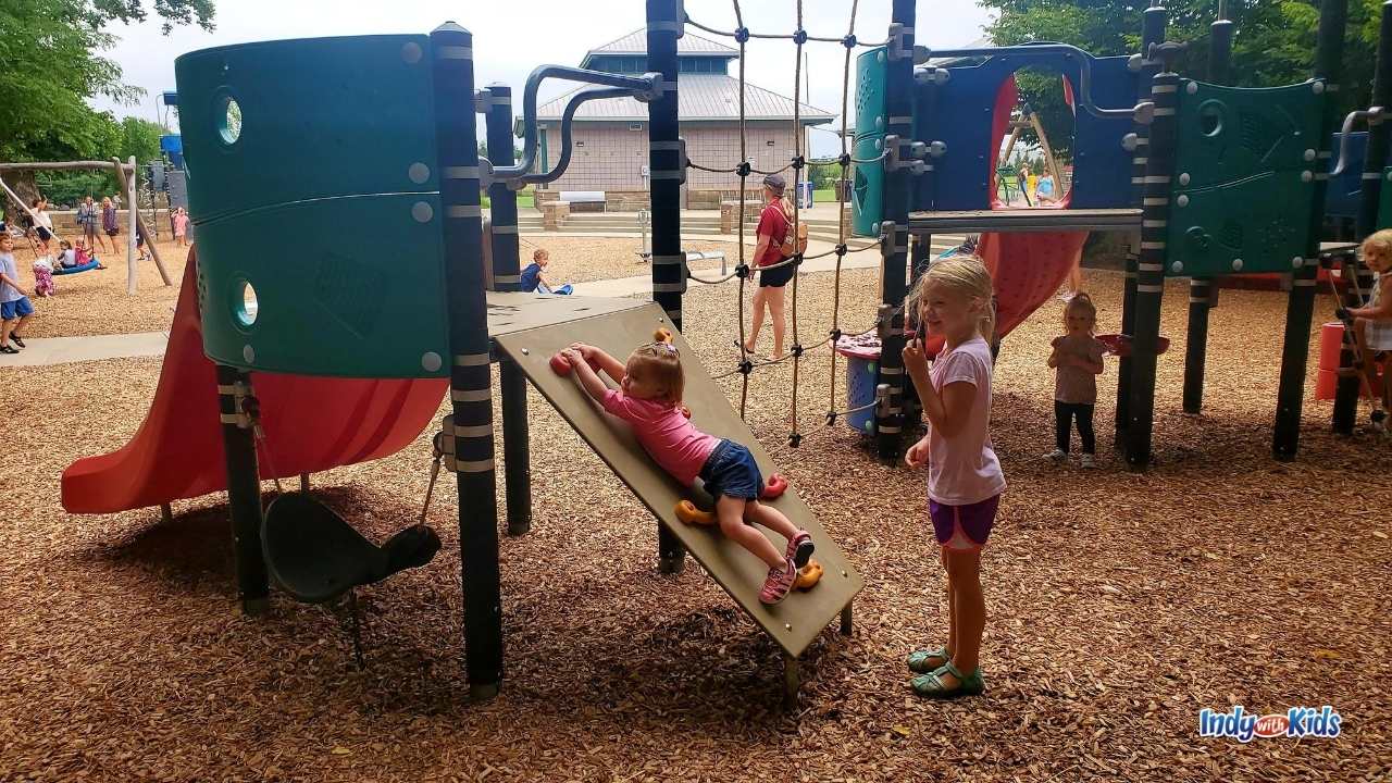 several children play in the toddler part of the playground at dillon park. one is climbing up a rock wall while others play on jungle gym over mulch.