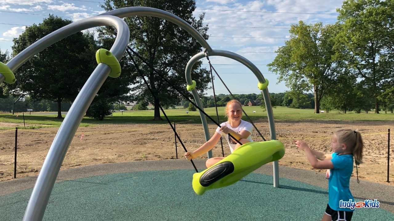 A girl sits on a circular swing while another pushes her at Independence Park Greenwood.