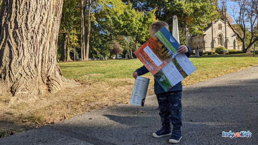 A child hold a container of leaves and a paper map of Crown Hill Cemetery's arboretum.