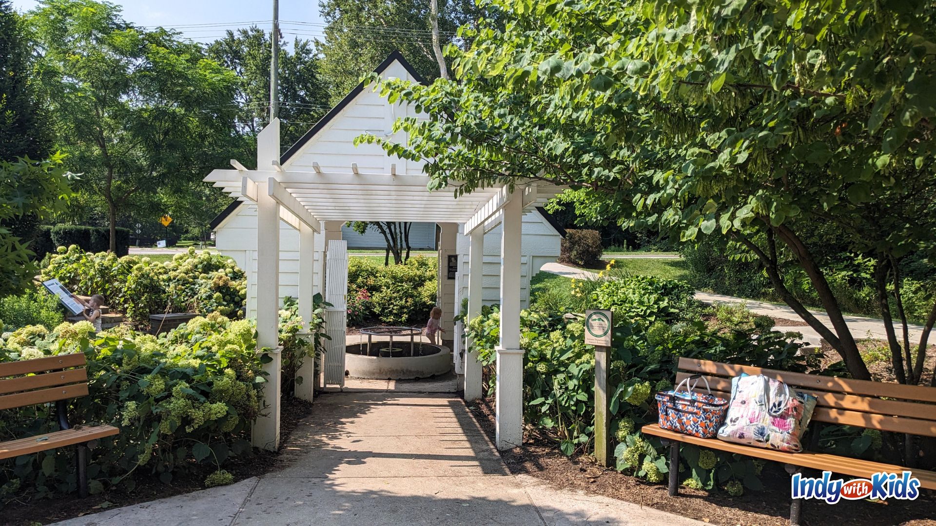 A white wooden house structure surrounded by flowers and bushes at Flowing Well Park in Carmel.