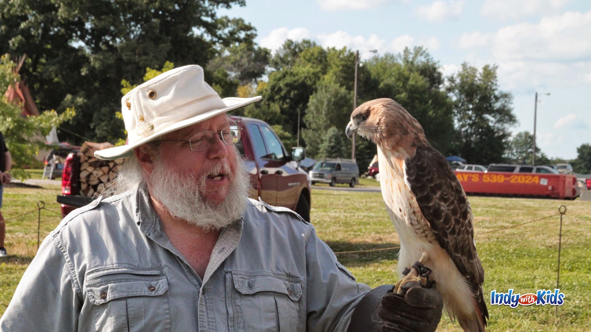 A man in a white hat holds a hawk on his gloved hand during an outdoor educational demonstration.
