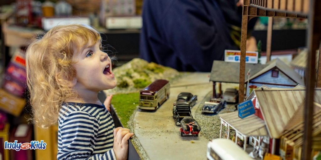 a little girl is happy and in awe of the model train track and city layout