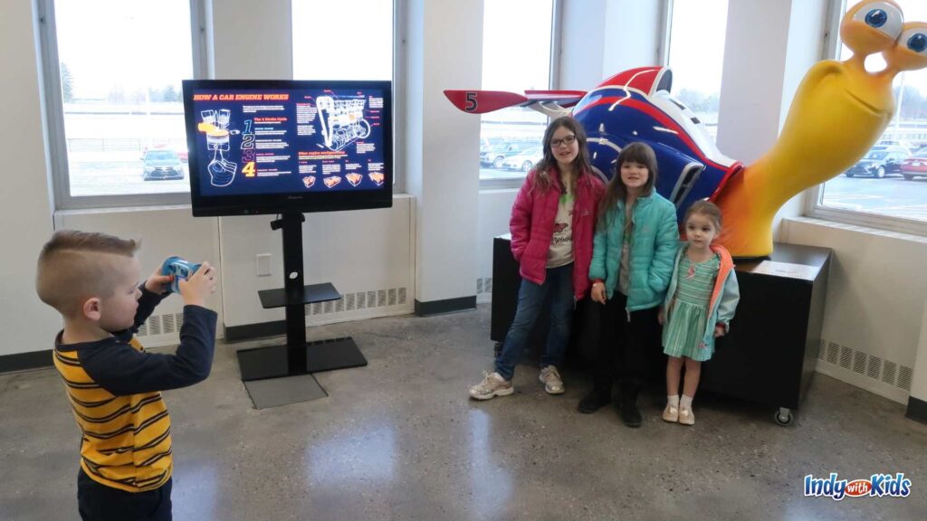 Children pose for a photo in front of a mascot at the Indianapolis Motor Speedway Museum.