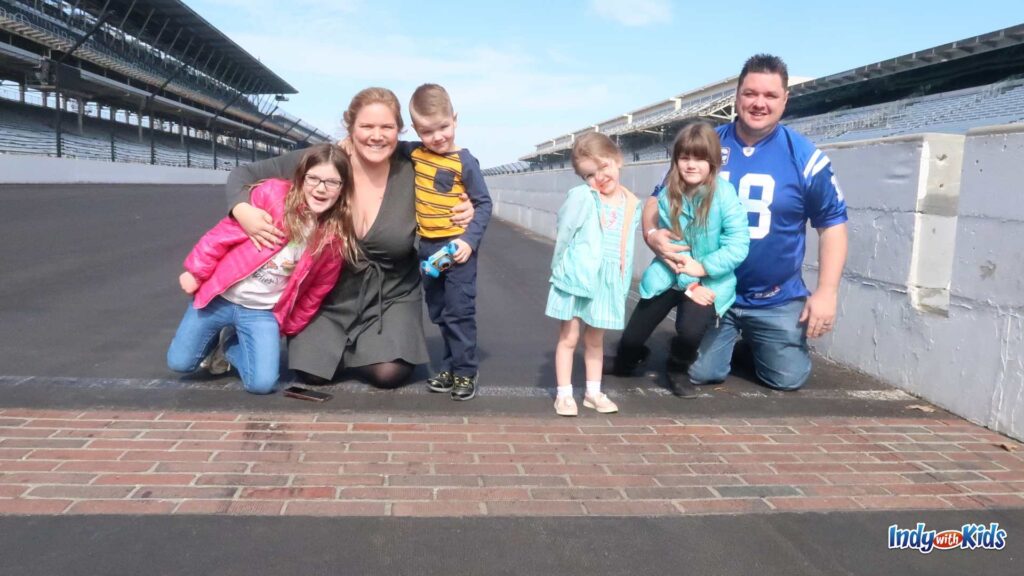A family of adults and children pose for a photo at the Yard of Bricks at the Indianapolis Motor Speedway finish line.