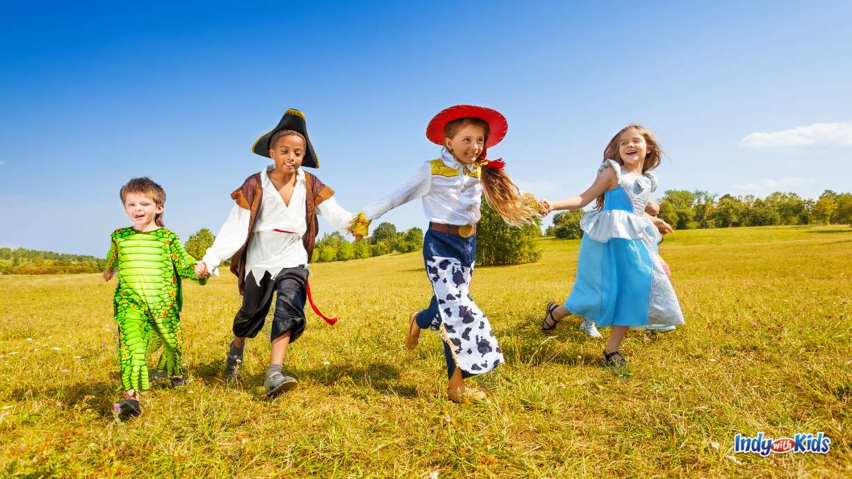 Halloween Fun Run: four children hold hands and run through a field, all dressed up in Halloween costumes