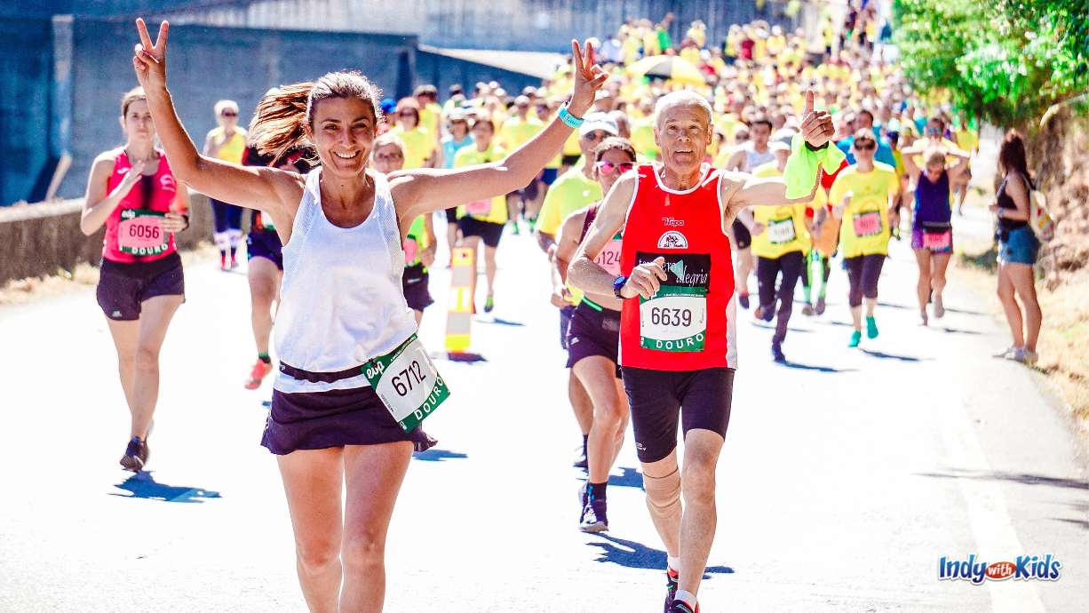 Halloween Fun Run: a sea of runner in the street running a race. the two in the forefront are giving a peace sign and thumbs up to the camera