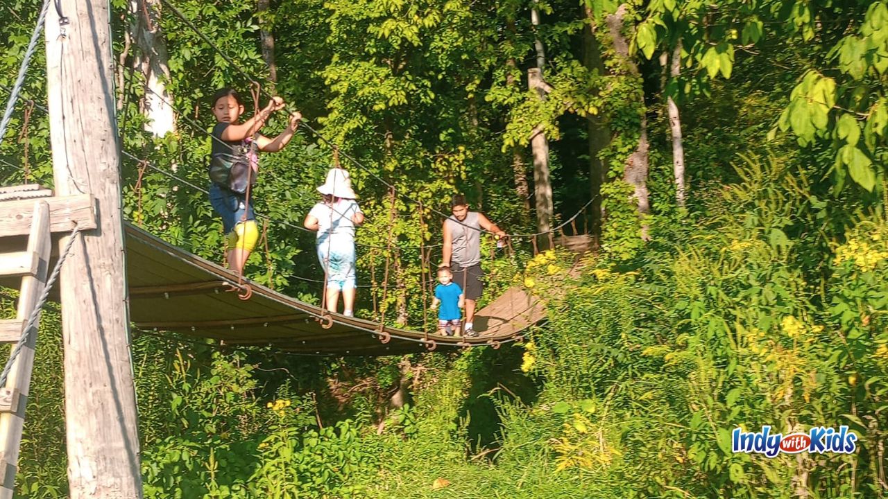 A family crosses a swinging bridge in the woods at Thornwood Nature Preserve.