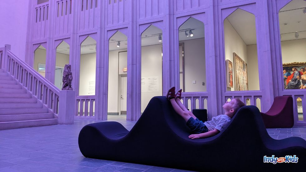 A boy looks up while reclining on a lounge chair in the Clowes Pavilion at Newfields.
