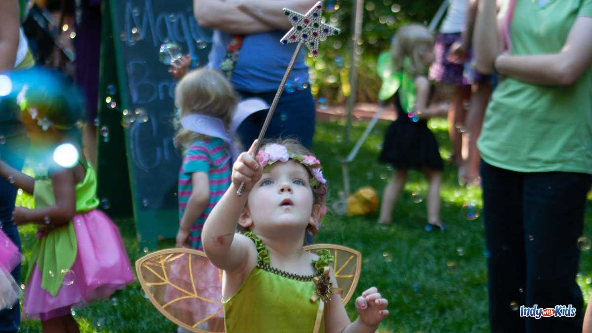 A child dressed as a fairy reaches a out a toy magic want to pop bubbles floating in the air at Faeries Sprites and Lights at Muncie's Minnetrista.