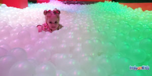Spring Break Activities Near Me: A child peeks out of a ball pit full of clear plastic balls.