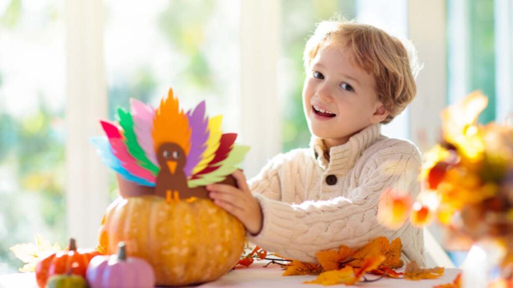 You've Been Gobbled | A Creative Thanksgiving Tradition of Giving for Kids: a boy smiles while holding his craft, a pumpkin with a turkey made of different colored construction paper on top