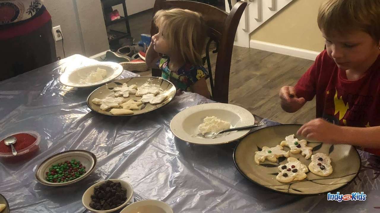 a little girl and little boy sits at a table in front of plates of cookies and bowls of toppings to decorate their cookies