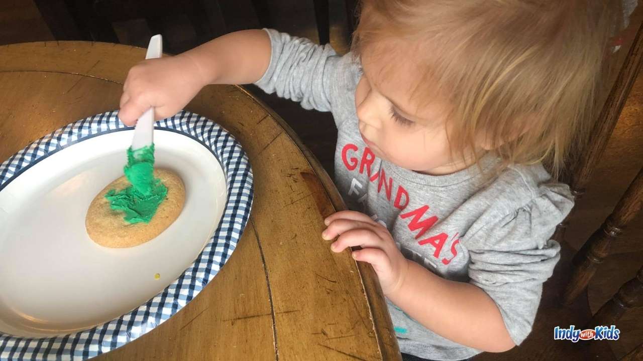 Holiday Treats: a little girl spreads green frosting on a sugar cookie