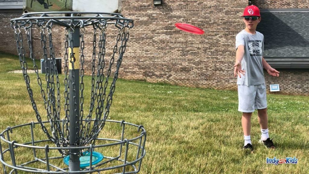 A child throws a disc into a disc golf Indianapolis course.