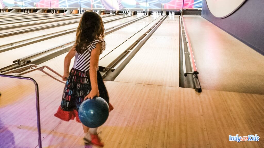 Girl is holding a bowling ball, ready to send it down the bowling alley during her kids bowl free session.