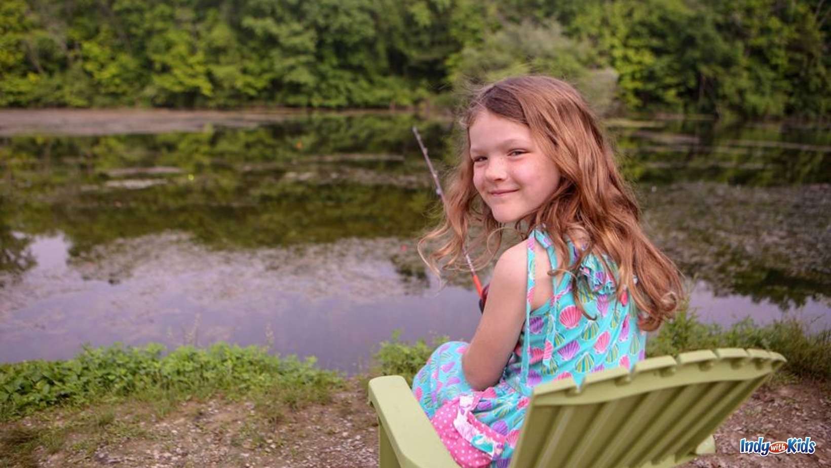 A girl sits in a plastic Adirondack chair while fishing at the Eagle Creek Fishing Derby. 