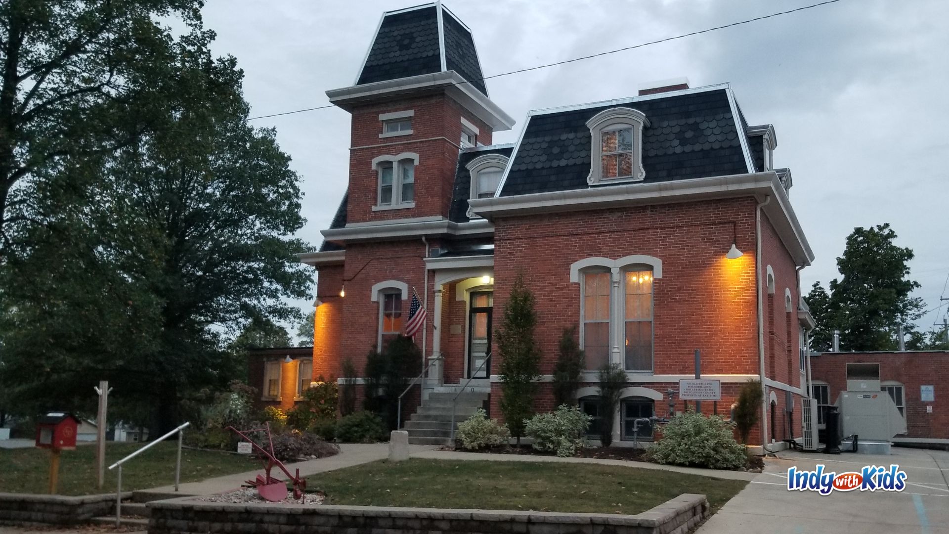 A red brick historic building with a tower, mansard roof, and American flag stands at dusk in Danville, Indiana.