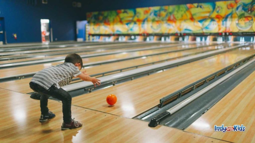 indoor things to do in Indianapolis for kids include this bowling alley where a boy is rolling a ball down the alley.