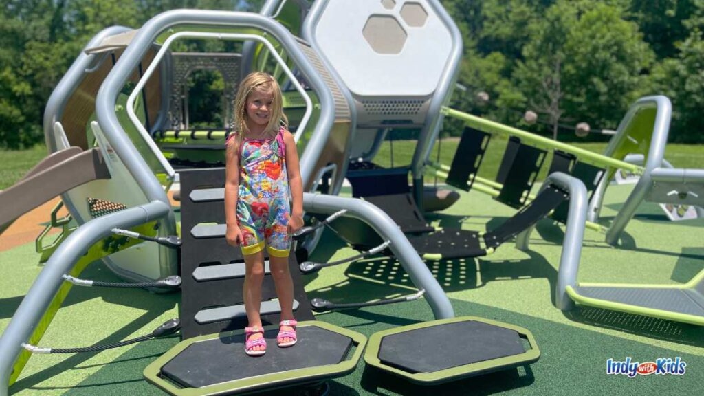 a little girl stands on a play structure at meadowlark park. there is a ladder behind her to an entrance to the inside of the low play structure.