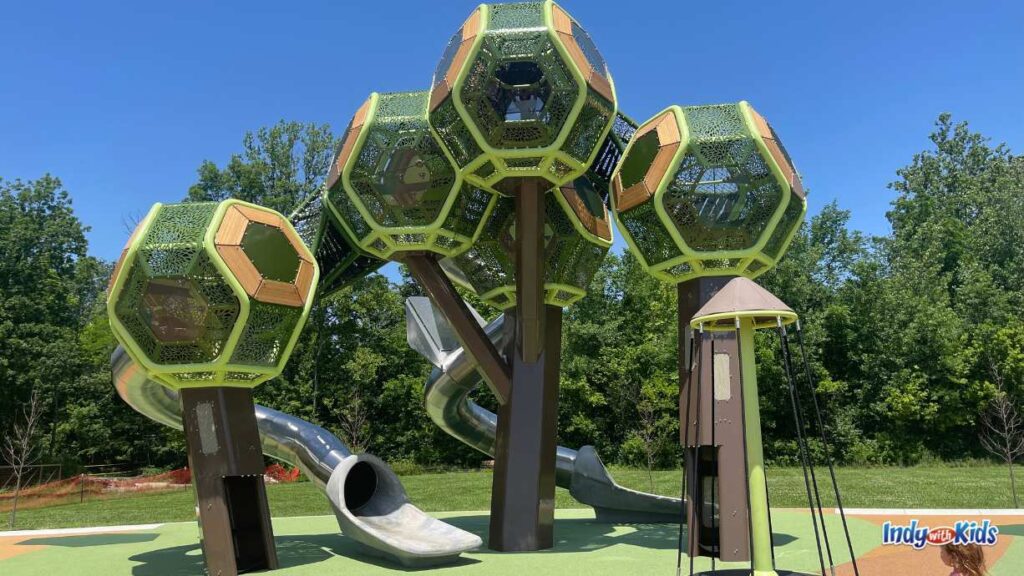 a very tall play structure resembling treetops with tree trunks to climb up inside at meadowlark park. there are silver slides coming down from the structure.
