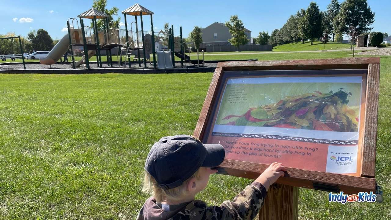 Story Walk Near Me: At a local park, a young boy points to the words on a sign displaying a page from a storybook.