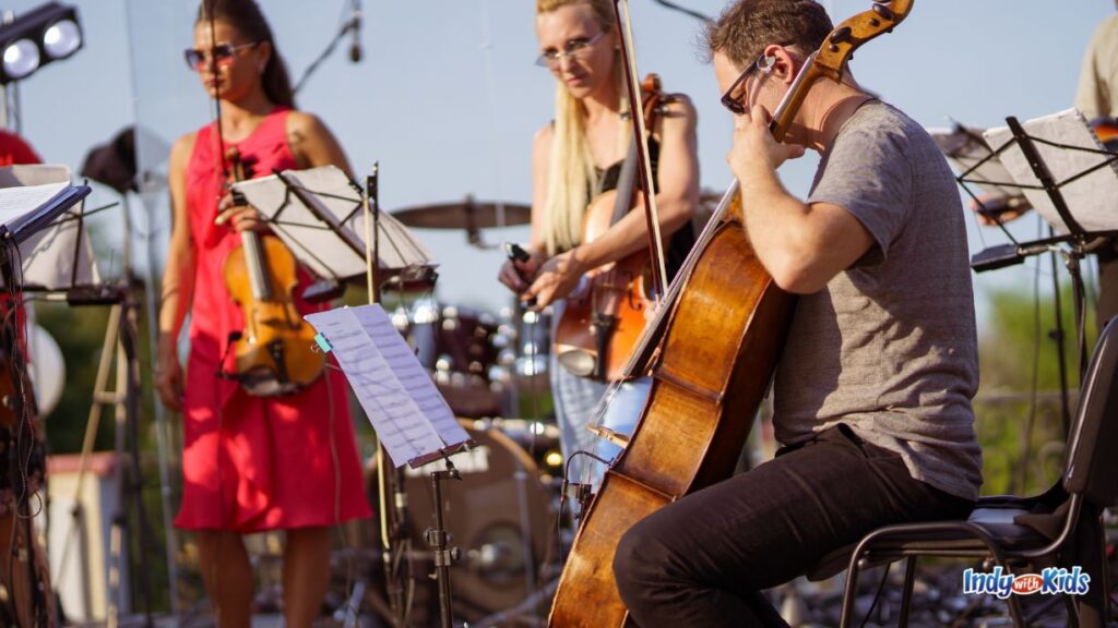 a quartet performs outdoors at a concert. two women with with violins are in the background and one man is in the foreground playing a larger bass