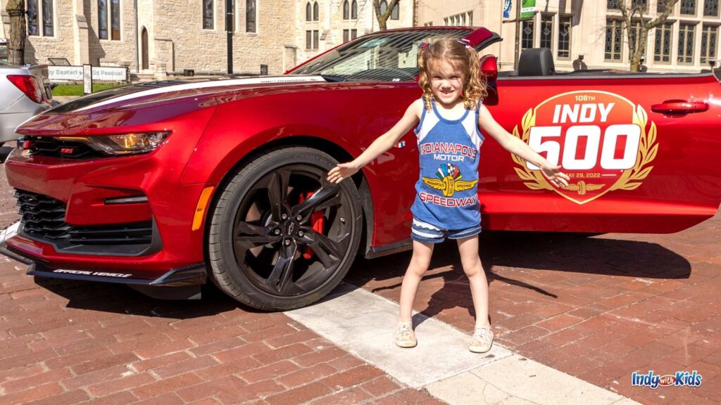 What to Wear to the Indy 500: a preschooler stands in front of the Indianapolis 500 pacecar wearing an Indianapolis Motor Speedway tank top and denim shorts.