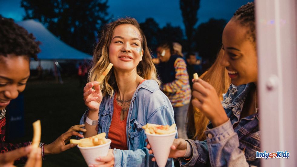 Festivals in Indiana: A group of teens laugh and snack on french fries at an outdoor carnival.