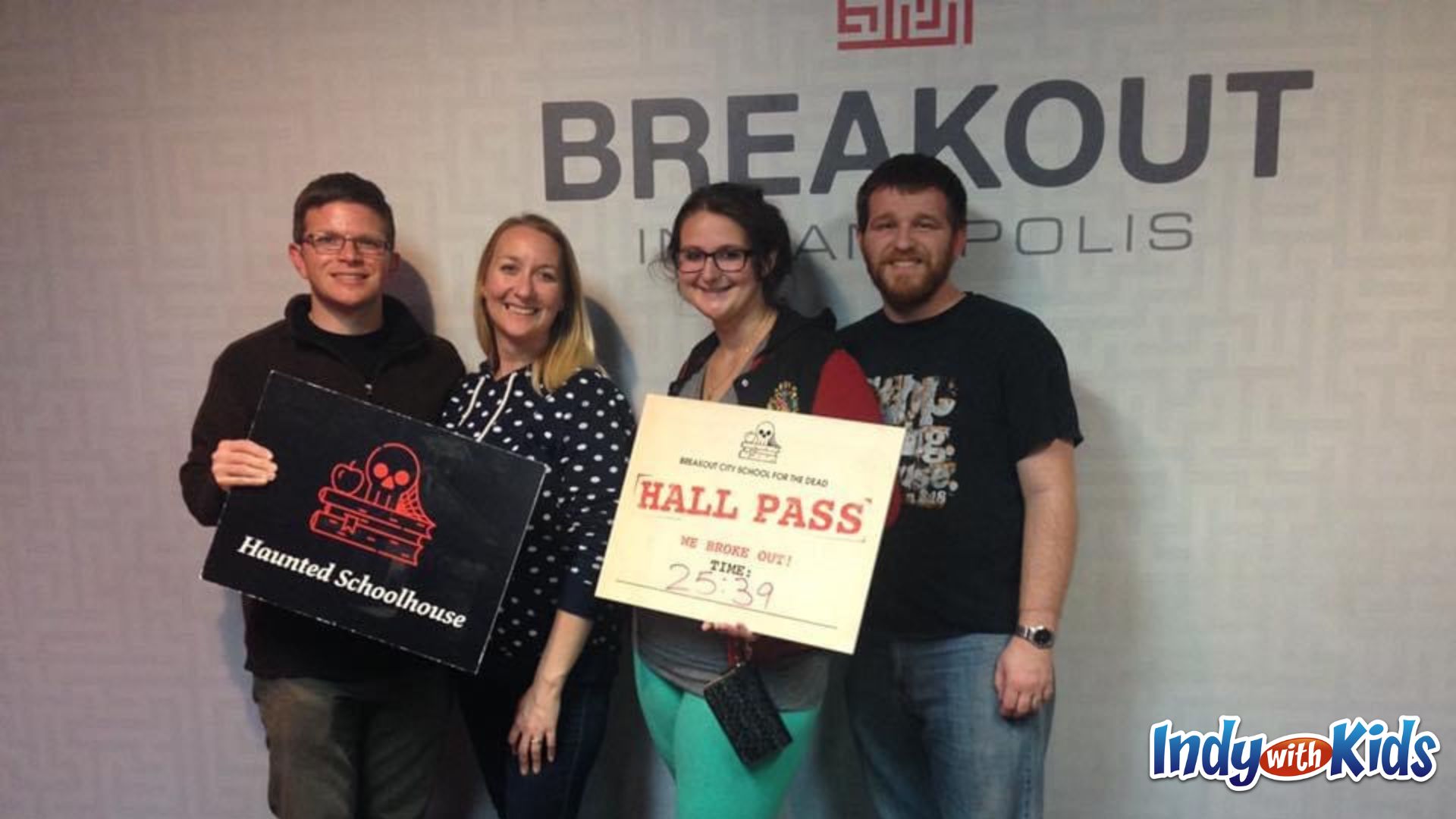 birthday activities for adults: two couples hold signs after completing an escape room. One says "haunted schoolhouse" and the other says "hall pass".