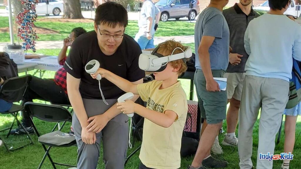an instructor helps a little boy wearing a VR headset and hand controllers at purdue spring fest
