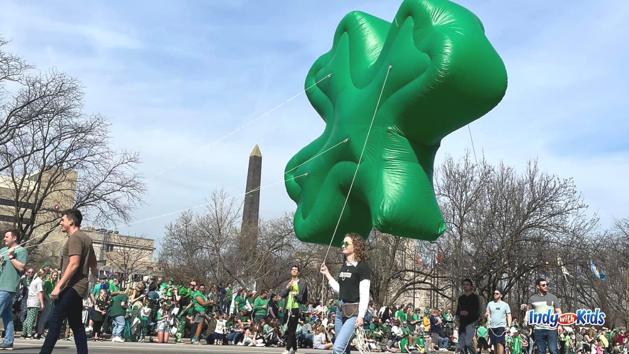 Four balloon handlers pull a giant floating shamrock parade balloon behind them at the Indianapolis Saint Patrick's Day Parade. The parade is one of our top March Date Ideas.