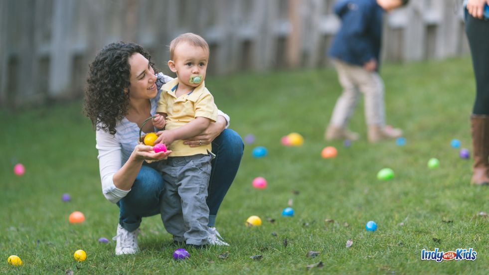Easter Egg Hunts in Indiana: A woman with brown curly hair encourages a toddler in a field full of plastic easter eggs.