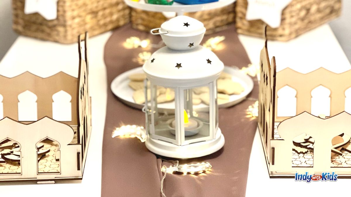 Ramadan Activities: A small white lantern with star patterns sits on a table alongside moon-shaped lights on a garland.