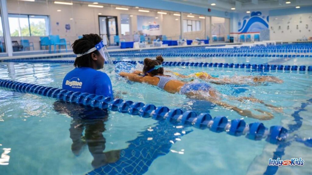 A swim instructor leads two swimmers in a lesson. Both swimmers have their heads face down in the water and appear to be floating