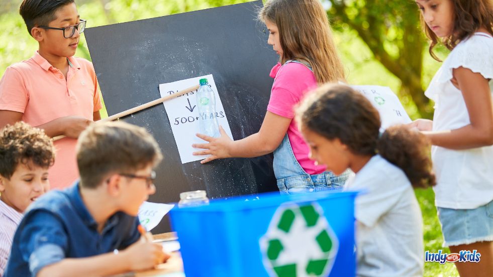 A group of children sort recyclable materials into blue bins with green recycling arrow symbols for Earth Day.