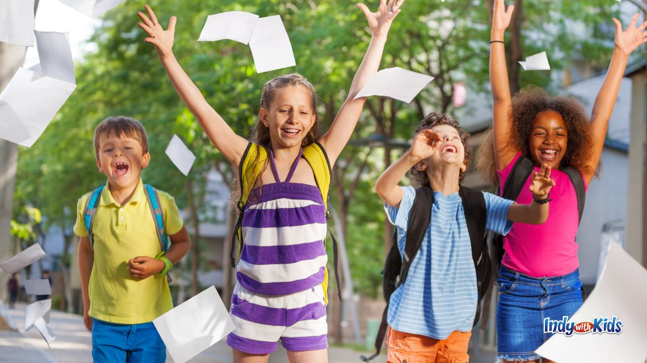 Four children with backpacks on throw white papers into the air and celebrate the last day of school