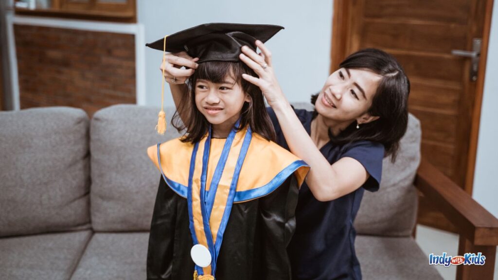 a mother adjusts the cap on a little girl wearing a graduation gown and salmon colored tassels