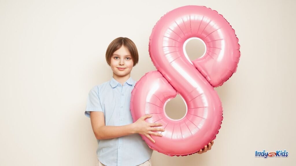 a child holds up a pink balloon of the number 7 to signify graduation 8th grade