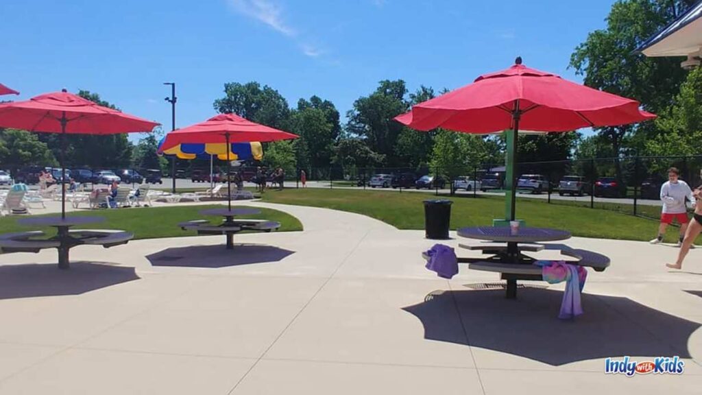 concessions area at seashore Waterpark consists of round table and benches covered by red umbrellas over concrete