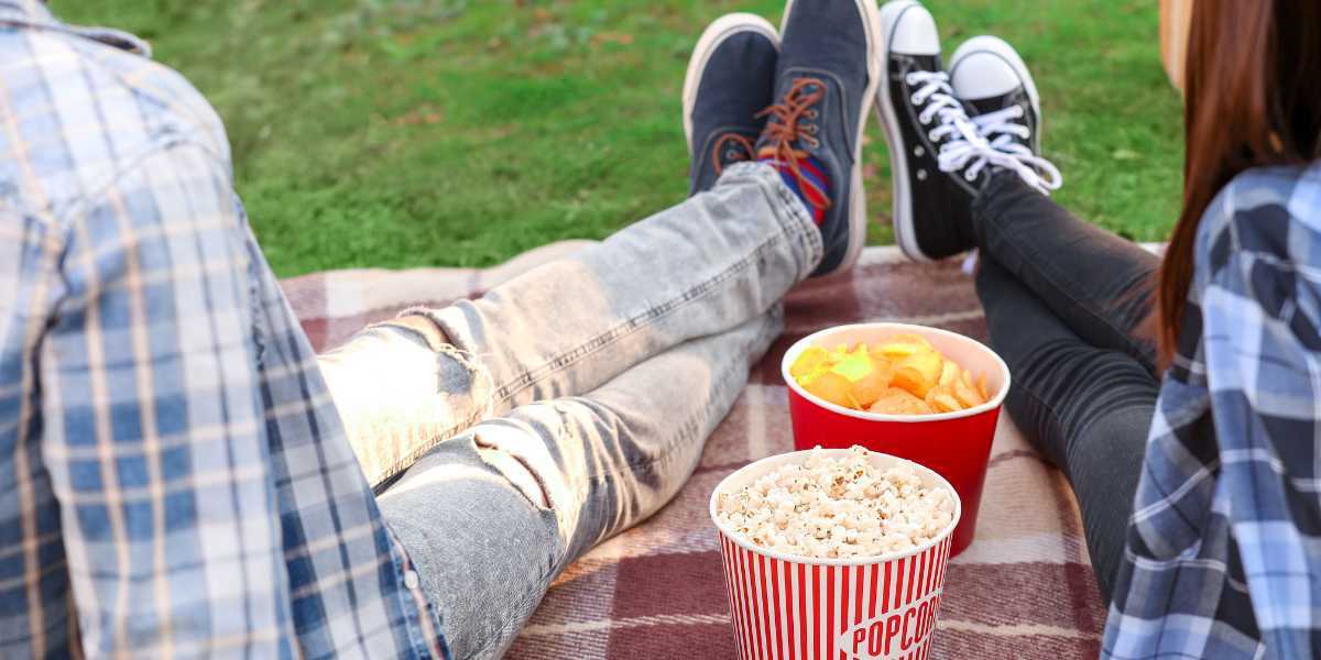 A couple relaxes on a blanket with popcorn and snacks to watch a film at Newfields Summer Nights movie series.