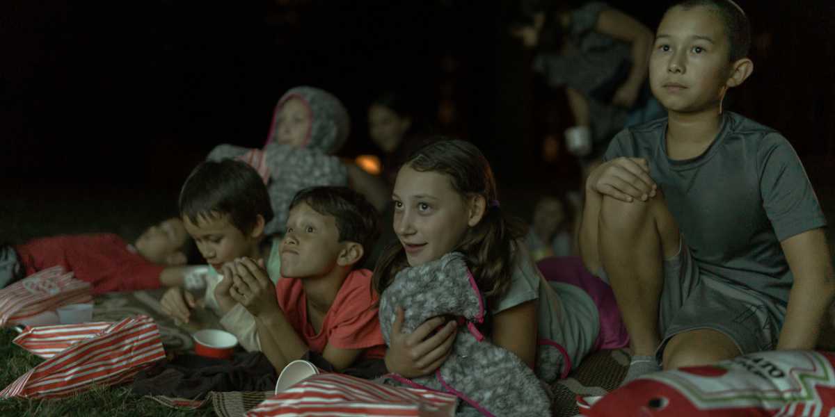 Kids sprawl on blankets with popcorn bags to watch a movie at Newfields Summer Nights film series.