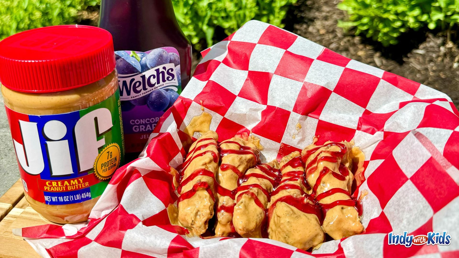 Indiana State Fair Food: A basket of chicken wings is lined with red and white checkered paper. The wings are covered in peanut butter and jelly and the containers for these condiments sit alongside the basket.