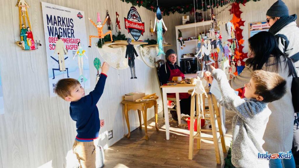 Carmel Christkindlmarkt: children explore wooden marionettes hanging from the ceiling