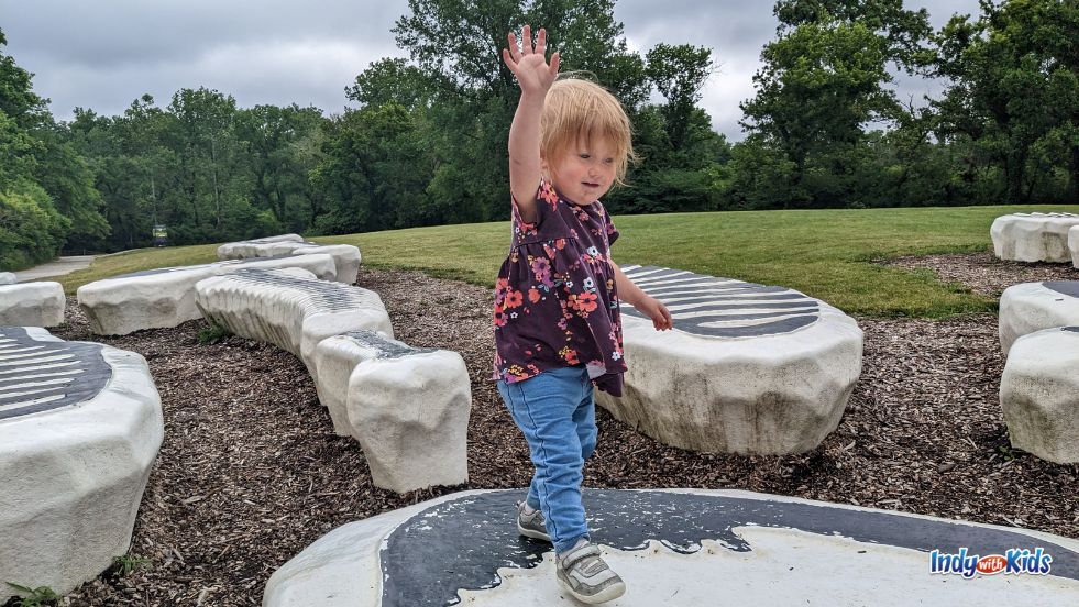 Outdoor Activities for Kids: A toddler balances on a portion of an oversized 3D model of a skeleton splayed out across a grassy area at Newfield's 100 Acres Art and Nature Park.