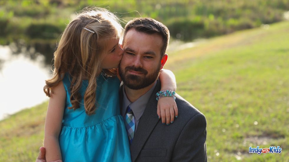 A child in formal wear kisses her father on the cheek on their way to a daddy daughter dance.