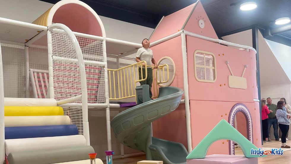 A boy stands at the top of a light green spiral slide descending from the pink children's playset at Urban Brew Cafe.