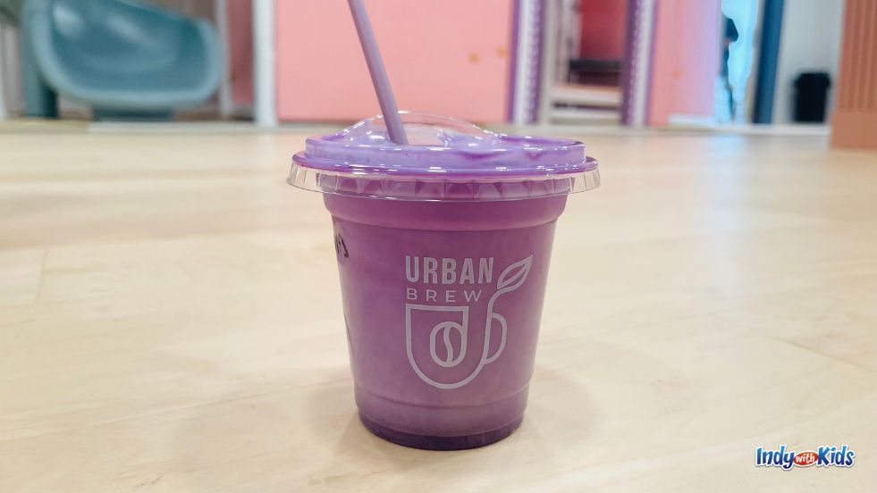 A plastic cup holding a creamy purple beverage sits on a wooden table at Urban Brew Cafe.