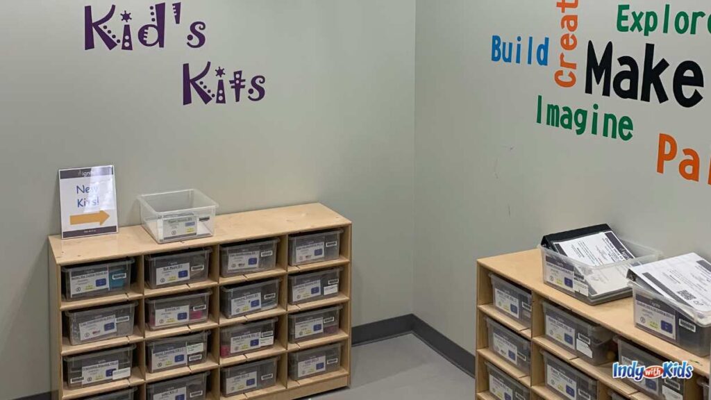 wooden cubbies hold plastic containers of kits to check out. the wall says kid's kits on one side and the other wall has steam kits