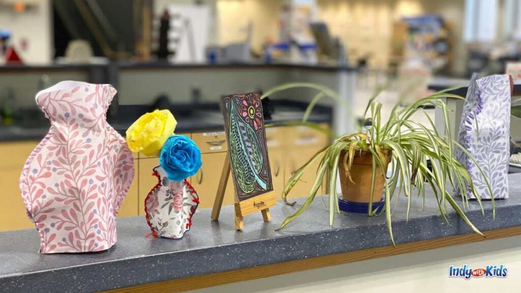 Various creations made at Ignite Studio are on display on a ledge, including sewn fabric vases, scratch art, and a plant