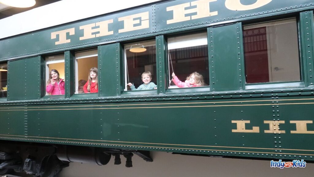 children peek out of the windows of a train car converted into a hotel